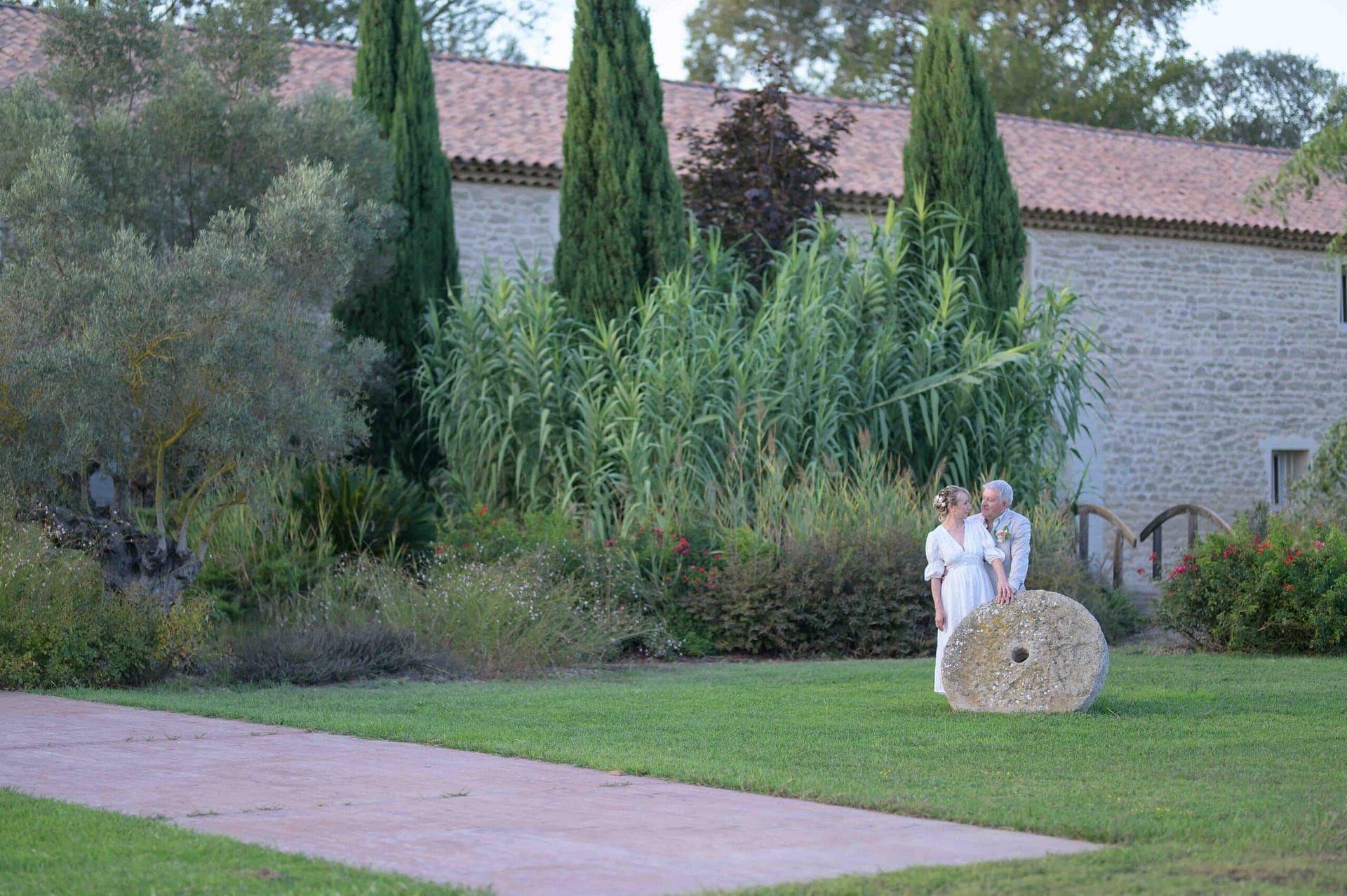 Mariés se regardant de loin au Mas Saint Gabriel à Marsillargues dans le Gard, avec arbres, pelouse, roue en pierre et mas en pierre
