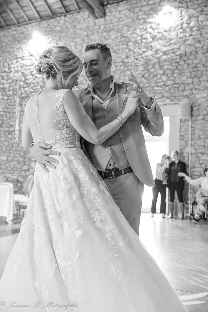 Les mariés dansent en noir et blanc ; le marié sourit largement en admirant son épouse