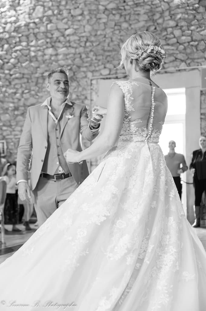 Les mariés dansent en noir et blanc ; la mariée de dos, à bout de bras, et le marié esquissant un léger sourire