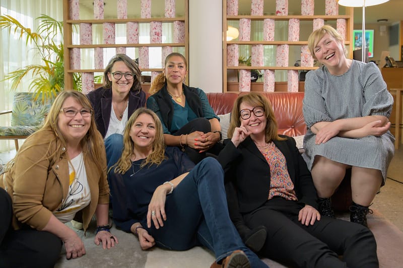 Six entrepreneuses sourient calmement ensemble lors du shooting professionnel au Greet Hôtel Montpellier, heureuses de se retrouver.